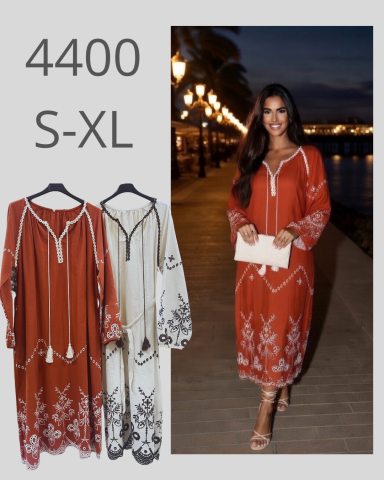 Mujer sonriente con vestido largo marrón y blanco, junto a otras prendas colgadas.