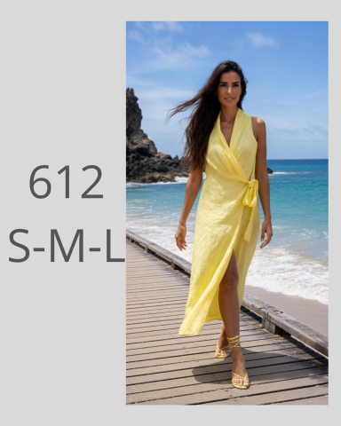 Mujer caminando por la playa con un vestido amarillo y sandalias en un entorno natural.