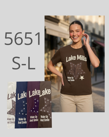 Mujer sonriente con camiseta marrón que dice "Lake Mills" en un entorno urbano.
