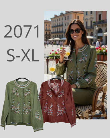 Mujer sonriente en un café, vistiendo una blusa bordada en verde y rojo, con un fondo urbano.