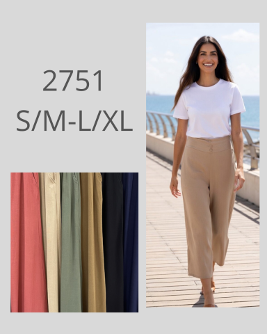 Mujer con camiseta blanca y pantalones beige caminando por un paseo marítimo.