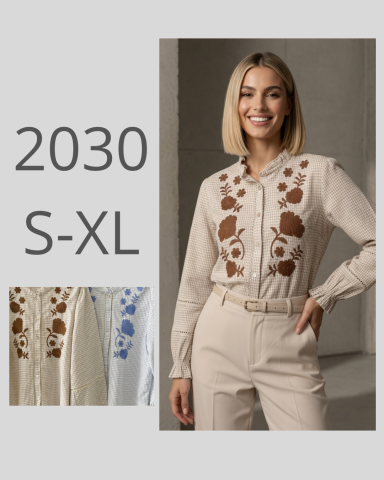Mujer sonriente con camisa elegante, bordados florales y pantalones claros.