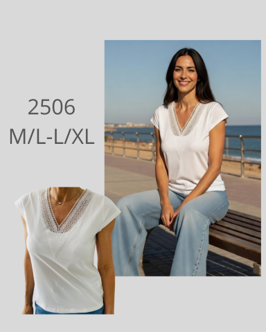 Mujer sentada en la playa con blusa blanca y jeans, fondo de mar y skyline urbano.