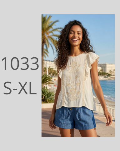 Mujer con blusa clara y pantalones cortos, sonriendo frente al mar y palmeras.