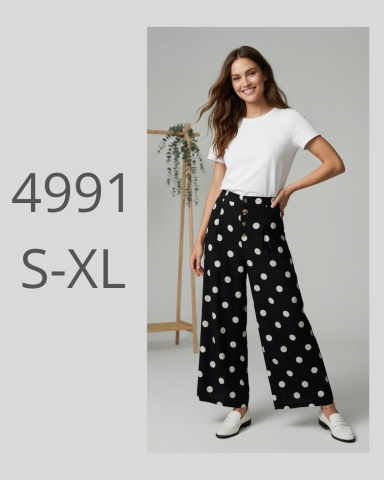 Mujer posando con blusa blanca y pantalones negros con lunares blancos.