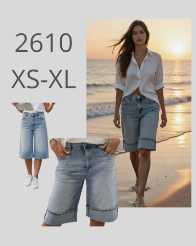 Mujer camina por la playa con pantalones cortos de mezclilla y camisa blanca.