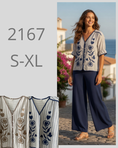Mujer con blusa bordada y pantalones oscuros, sonriente en un entorno urbano.