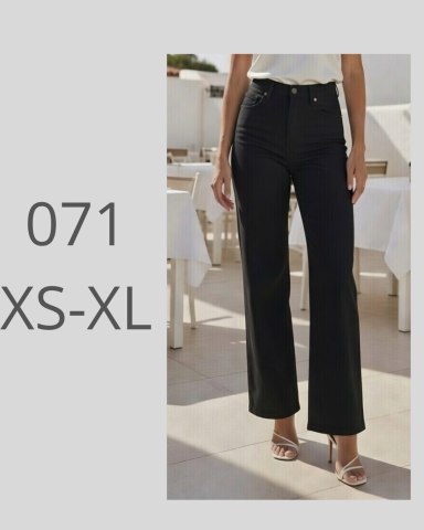 Mujer de pie con pantalones negros de corte recto y sandalias en un entorno exterior.