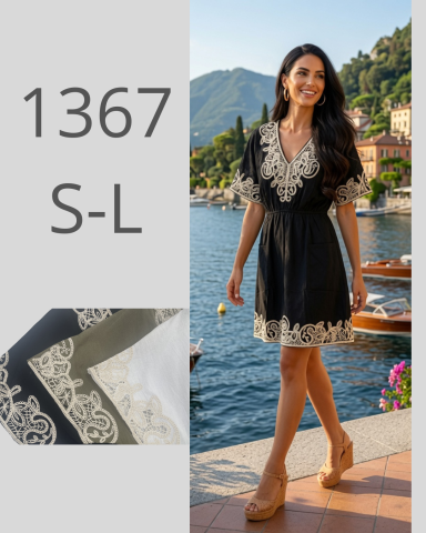 Mujer sonriente con vestido negro y blanco, de pie junto a un lago. Fondo montañoso.