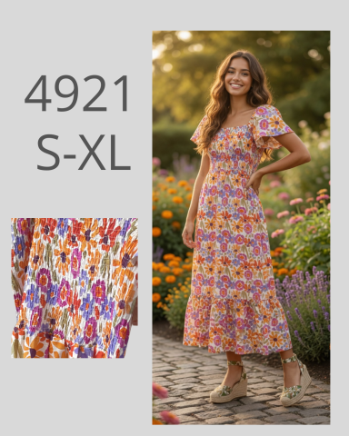 Mujer de pie en un vestido floral entre flores coloridas, sonriendo y con cabello suelto.