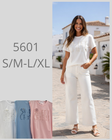 Mujer sonriendo con camiseta blanca y pantalones claros, posando en una calle soleada.