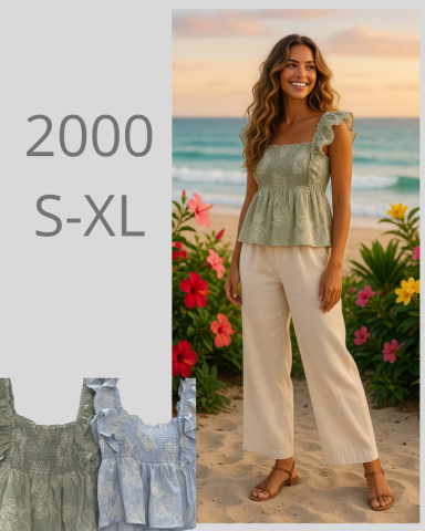 Mujer sonriente en la playa con blusa verde y pantalones claros, flores de fondo.