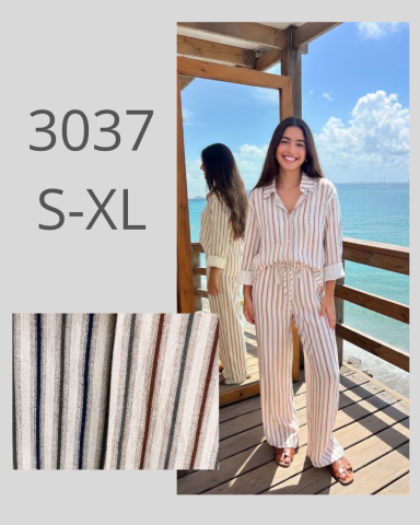 Mujer sonriente con un conjunto claro, de pie junto al mar, mostrando variedad de tejidos.