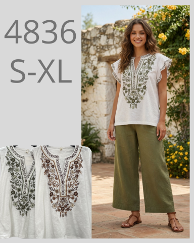 Mujer con blusa blanca bordada y pantalones verdes, de pie en un entorno natural.