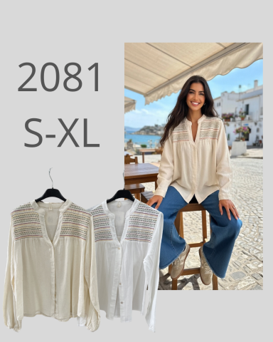 Modelo sonriente vistiendo una camisa blanca frente a un fondo de playa. Camisa disponible S-XL.