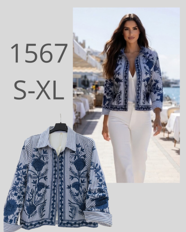 Mujer con chaqueta azul y blanca caminando junto a una terraza, con un fondo costero.