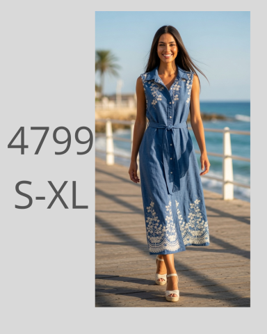 Mujer sonriente en vestido azul largo con bordados, paseando junto al mar.