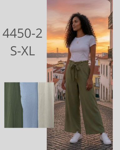 Mujer con pantalones anchos y camiseta, fondo de atardecer en una ciudad.