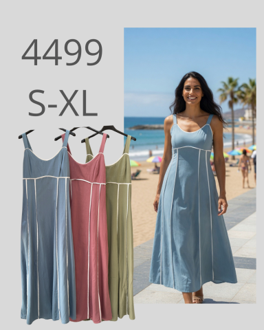 Mujer sonriente en la playa con vestido largo en tonos azul, rosa y verde.