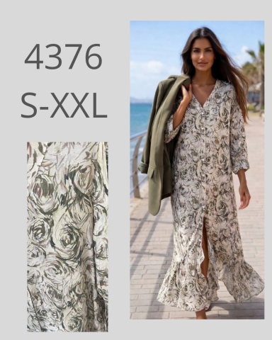 Mujer con vestido floral largo y abrigo, caminando junto al mar en un día soleado.