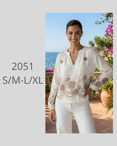 Blusa blanca con bordado marrón, cuello en V y mangas largas, vista al mar.