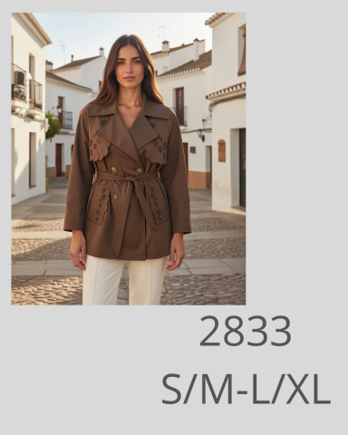 Mujer con abrigo marrón y pantalones claros, en un entorno urbano al aire libre.