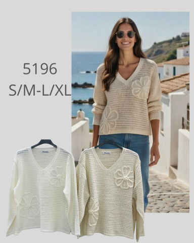 Mujer sonriente con un suéter claro, posando en un entorno costero. Suéteres colgados a un lado.