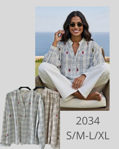 Mujer sonriente con camisa de cuadros y pantalones claros, sentada al aire libre.