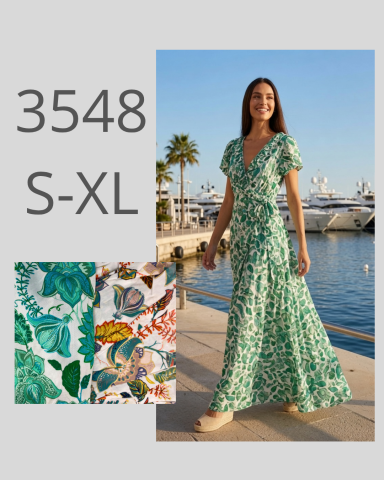 Mujer sonriendo con vestido largo de flores, junto al mar y yates de fondo.