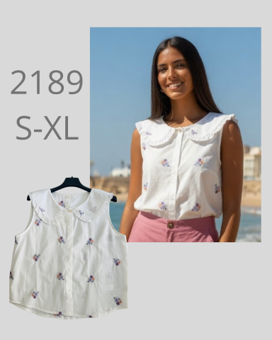 Mujer sonriente en blusa blanca con estampado, fondo de playa. Tallas S-XL.