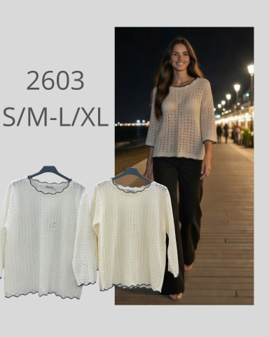 Mujer modelo con blusa clara y pantalones oscuros, caminando por un paseo iluminado.