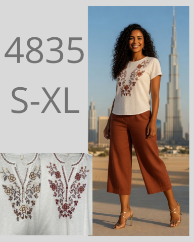 Mujer modelando una blusa bordada con pantalones marrones, fondo con la Torre de Dubai.