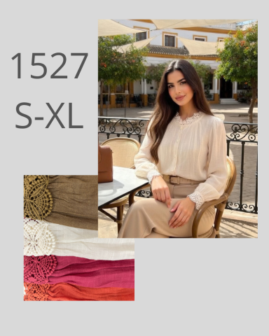 Mujer sentada en una terraza con blusa clara y falda, rodeada de plantas y edificios.