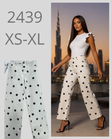 Modelo con ropa de pantalones blancos con puntos negros y blusa blanca, de fondo un paisaje urbano.