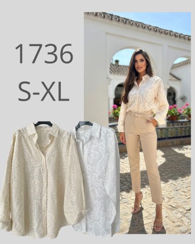Mujer con blusa clara y pantalones beige, rodeada de flores y arquitectura blanca.