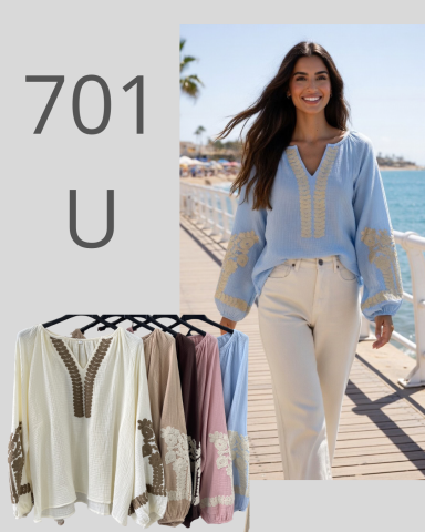 Mujer sonriente luciendo blusa azul con detalles en los brazos, junto al mar.