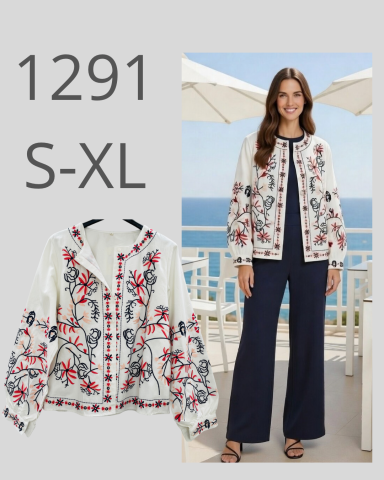 Mujer de pie con chaqueta bordada, pantalones oscuros y fondo de terraza con vista al mar.