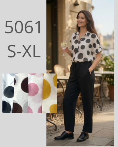 Mujer sonriente con blusa de lunares y pantalones oscuros, sosteniendo una bebida.