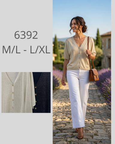 Mujer sonriente con blusa beige y pantalones blancos, caminando por un sendero de lavanda.