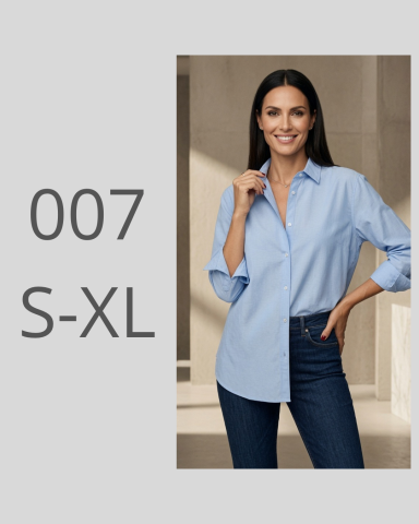 Mujer sonriente con camisa azul claro y jeans, de pie en un entorno luminoso.