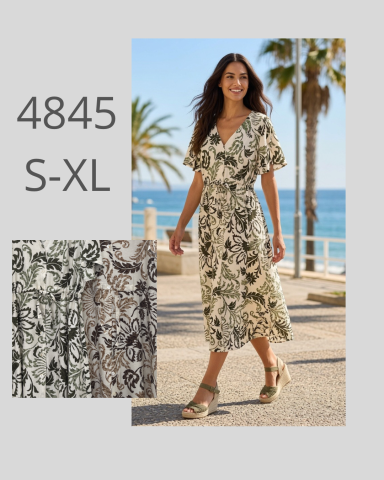 Mujer sonriente en vestido largo y sandalias, paseando al lado del mar y palmeras.