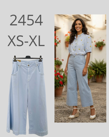 Mujer de pie con blusa y pantalones claros, fondo con plantas y flores. Tamaños XS-XL.