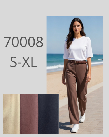 Mujer con camiseta blanca y pantalones marrones caminando por la playa.