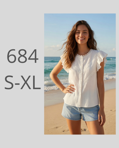 Mujer sonriente en la playa, lleva una blusa blanca y pantalones cortos de mezclilla.