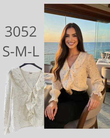 Mujer sonriente con blusa clara y lazos, sentada junto a una ventana con vista al mar.