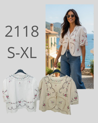 Mujer sonriente con blusa floral en paisajística costera; blusas blancas y beige abajo.