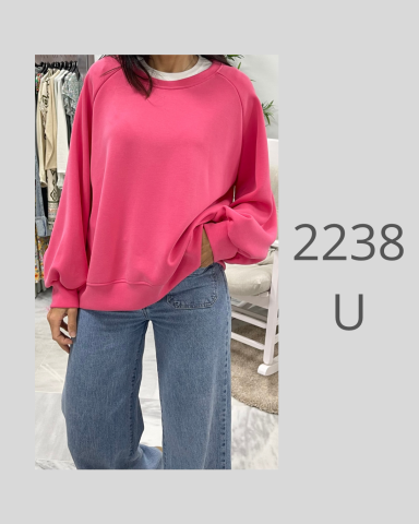 Una persona viste un suéter rosa con mangas holgadas y pantalones vaqueros.