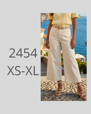 Mujer con pantalones anchos claros y blusa amarilla frente al mar.