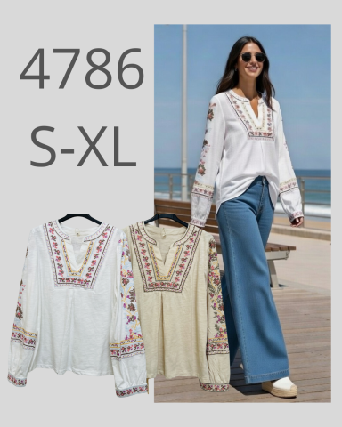 Mujer sonriente con blusa blanca y pantalones azules, en un entorno costero.