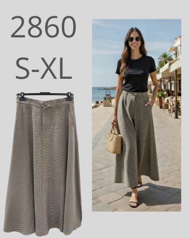 Mujer con pantalones anchos y camiseta negra, caminando junto a la playa.